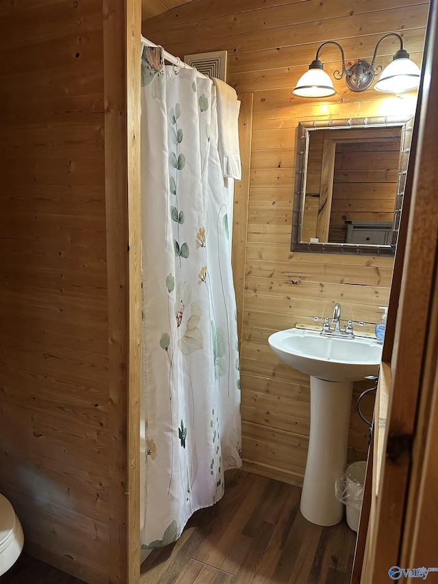 full bath with curtained shower, a sink, wooden walls, and wood finished floors