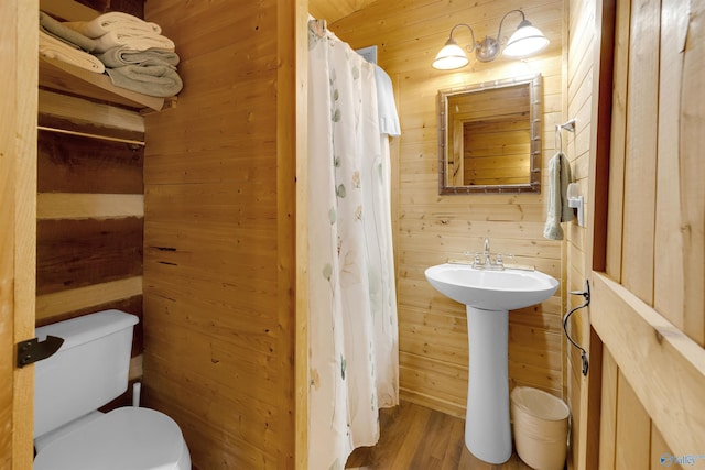 bathroom with a shower with shower curtain, wood walls, toilet, and wood finished floors