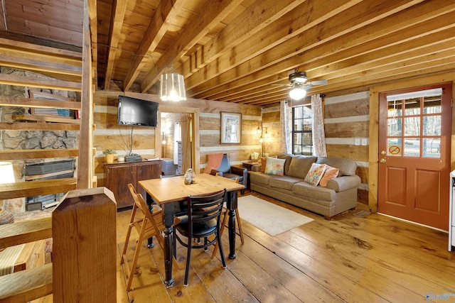 dining space with light wood finished floors, wood walls, a stone fireplace, wooden ceiling, and beamed ceiling