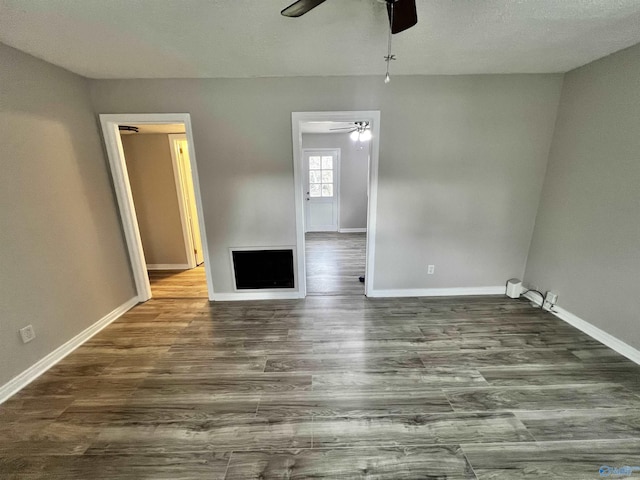 spare room featuring a textured ceiling, ceiling fan, dark hardwood / wood-style flooring, and a fireplace