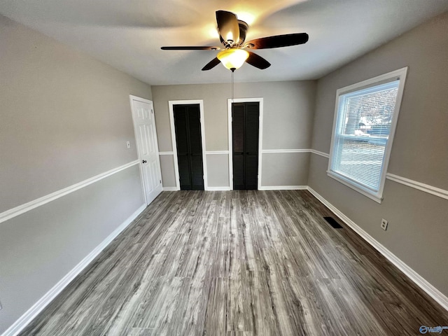 unfurnished bedroom featuring ceiling fan, wood-type flooring, and multiple closets