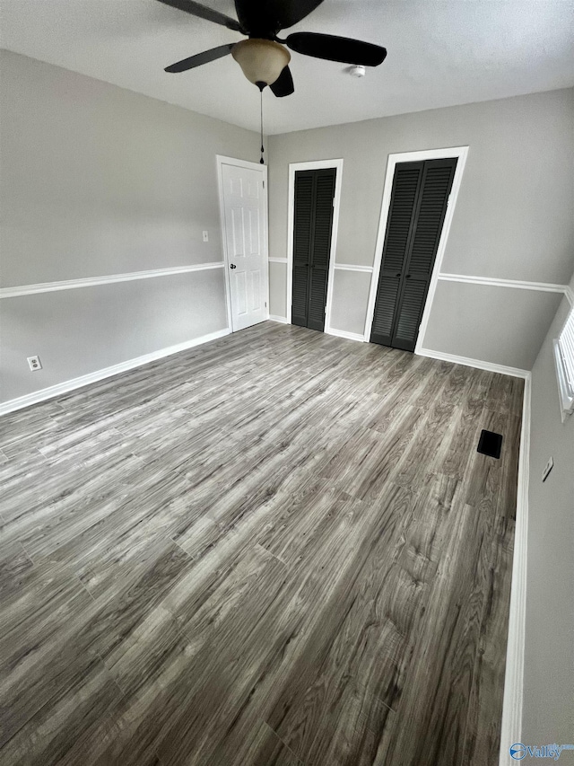 unfurnished bedroom featuring ceiling fan, two closets, and hardwood / wood-style flooring