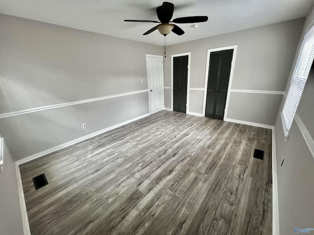 unfurnished bedroom with multiple closets, ceiling fan, and hardwood / wood-style floors