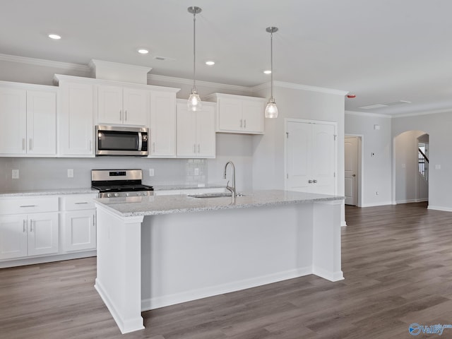 kitchen with arched walkways, white cabinets, a kitchen island with sink, a sink, and stainless steel appliances