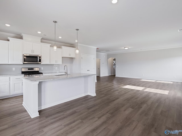 kitchen featuring arched walkways, a sink, stainless steel appliances, open floor plan, and a center island with sink