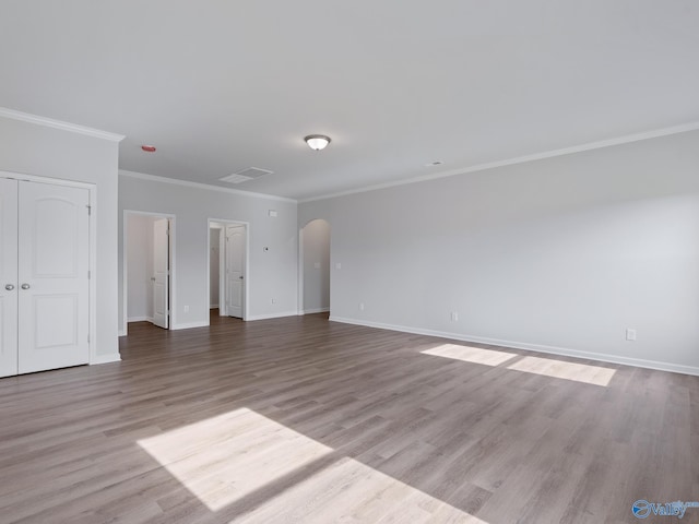 unfurnished living room with baseboards, crown molding, visible vents, arched walkways, and wood finished floors
