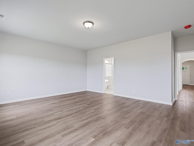 spare room with arched walkways, visible vents, baseboards, and wood finished floors