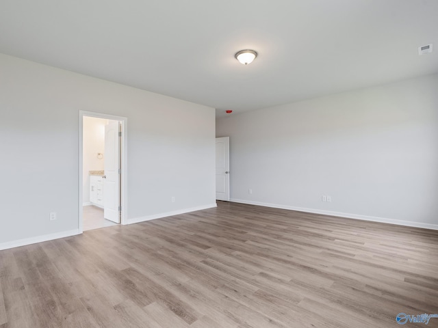 interior space with light wood-style flooring, baseboards, visible vents, and connected bathroom