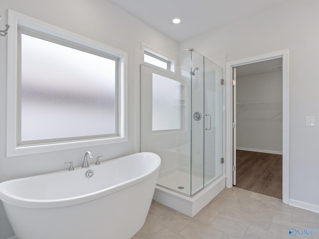 bathroom with a shower stall, a walk in closet, tile patterned flooring, and a soaking tub