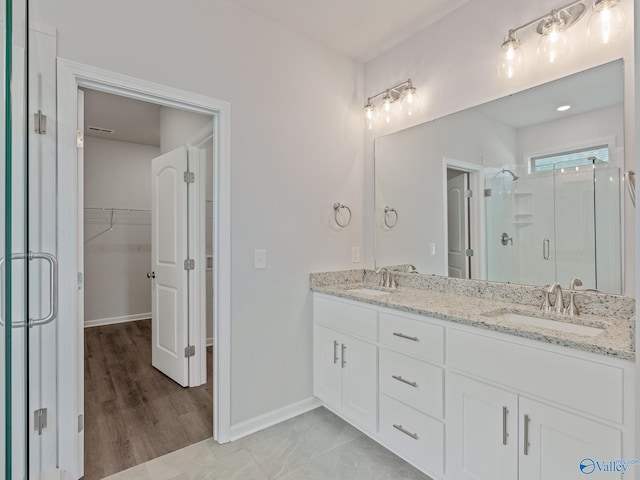 bathroom featuring a sink, a walk in closet, a shower stall, and double vanity