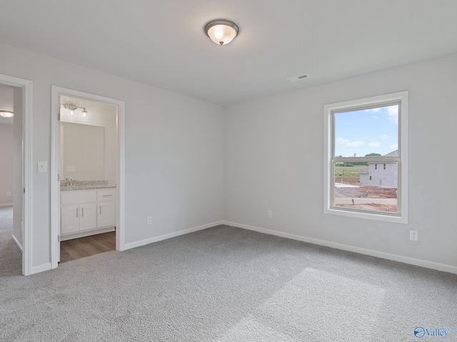 unfurnished bedroom featuring ensuite bath, visible vents, baseboards, and carpet floors