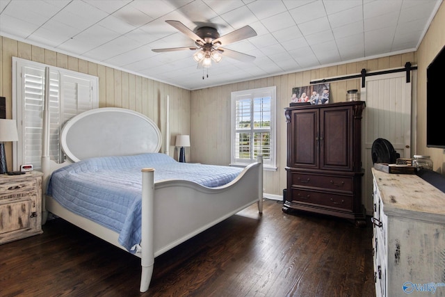bedroom with baseboards, a barn door, dark wood-style floors, and a ceiling fan