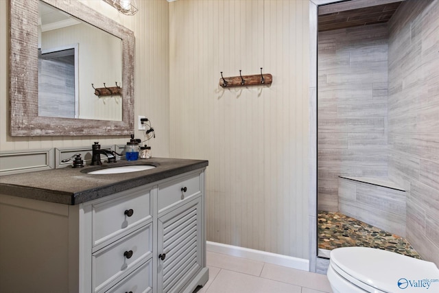 bathroom with vanity, a tile shower, toilet, baseboards, and tile patterned floors