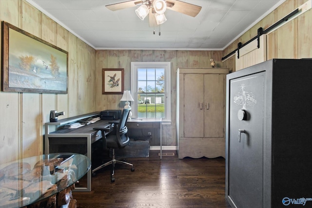 office featuring dark wood-style flooring, wooden walls, ceiling fan, ornamental molding, and a barn door
