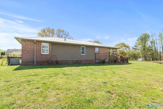 back of property featuring crawl space, metal roof, brick siding, and a yard