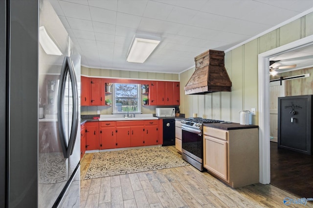 kitchen featuring light wood-style flooring, stainless steel appliances, a sink, custom range hood, and red cabinetry