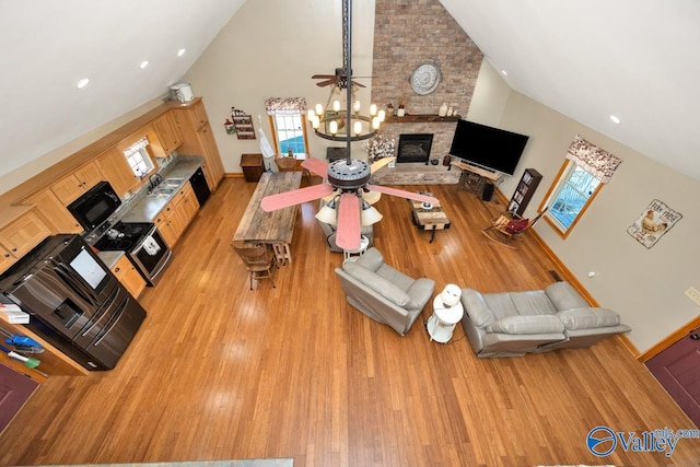 interior space featuring ceiling fan, a fireplace, high vaulted ceiling, and light hardwood / wood-style flooring