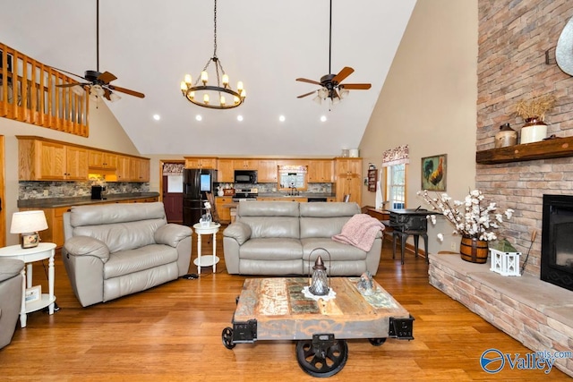 living room featuring ceiling fan, light hardwood / wood-style floors, a brick fireplace, and a high ceiling