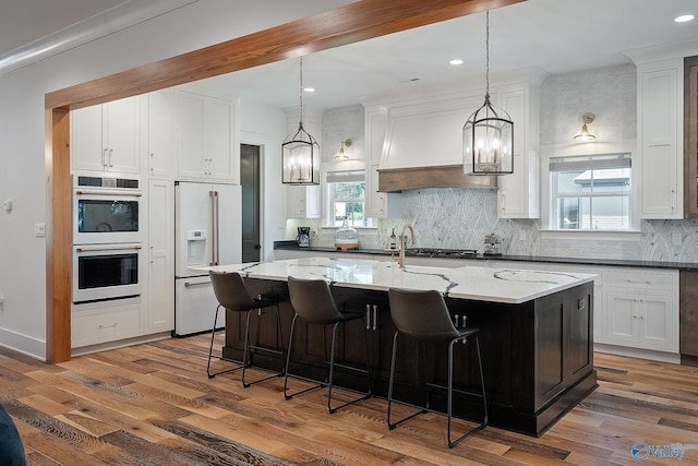 kitchen featuring stainless steel appliances, hanging light fixtures, an island with sink, dark stone countertops, and hardwood / wood-style flooring