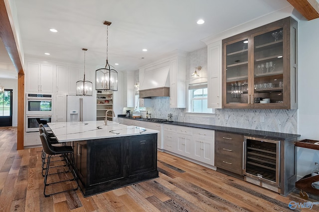 kitchen with white cabinets, beverage cooler, premium range hood, hardwood / wood-style floors, and appliances with stainless steel finishes