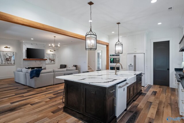 kitchen featuring white appliances, a center island with sink, light stone counters, hanging light fixtures, and dark hardwood / wood-style floors