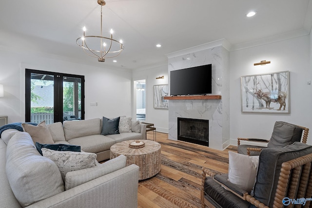 living room with a notable chandelier, crown molding, french doors, light hardwood / wood-style floors, and a premium fireplace