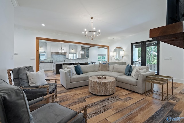 living room with ornamental molding, sink, an inviting chandelier, and hardwood / wood-style floors