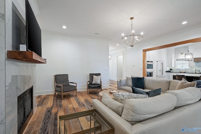 living room with a high end fireplace, crown molding, a chandelier, and hardwood / wood-style flooring