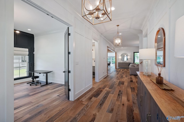 corridor featuring ornamental molding, dark hardwood / wood-style flooring, an inviting chandelier, and plenty of natural light