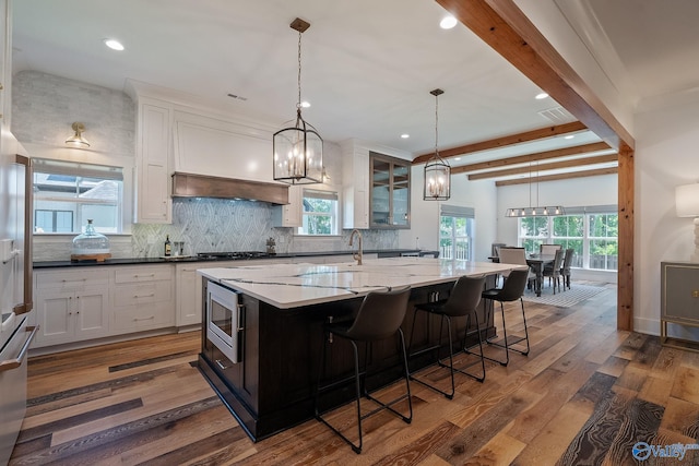 kitchen with decorative light fixtures, white cabinets, beamed ceiling, a kitchen island, and dark wood-type flooring