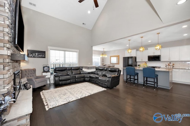 living room featuring ceiling fan, high vaulted ceiling, dark wood-type flooring, and a fireplace