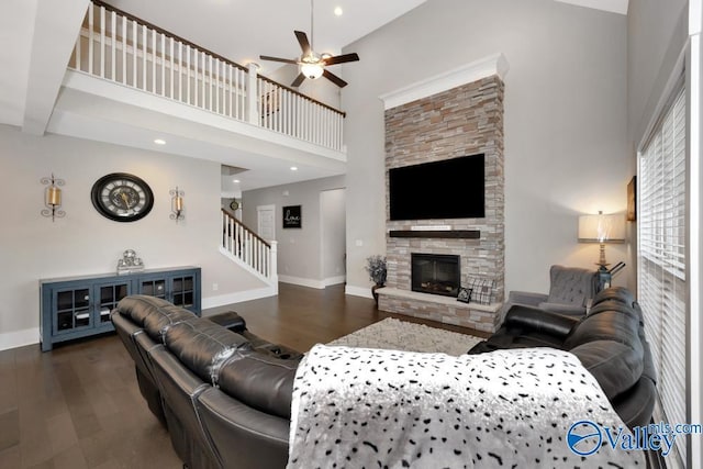 living room with dark wood-type flooring, ceiling fan, a fireplace, and a high ceiling