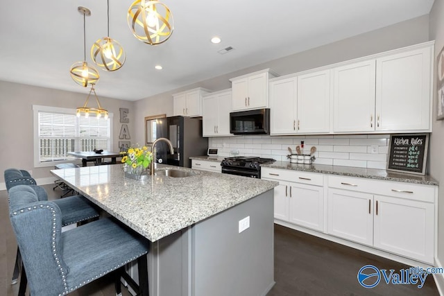 kitchen featuring white cabinetry, an island with sink, pendant lighting, light stone countertops, and black appliances