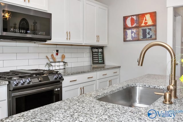 kitchen with gas range, sink, white cabinets, and decorative backsplash