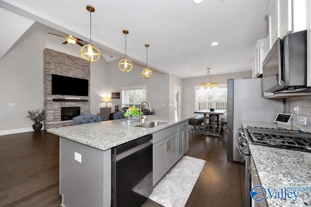 kitchen featuring sink, light stone counters, decorative light fixtures, a center island with sink, and stainless steel appliances