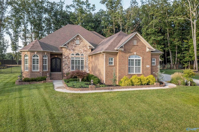 view of front of house with stone siding, brick siding, a front yard, and fence