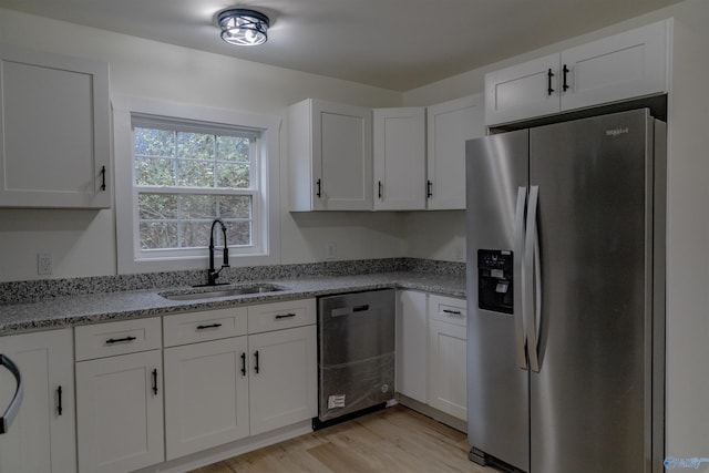 kitchen featuring appliances with stainless steel finishes, sink, white cabinets, light stone countertops, and light wood-type flooring