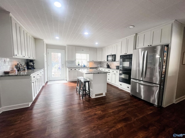 kitchen featuring white cabinetry, a kitchen breakfast bar, a center island, black appliances, and light stone countertops