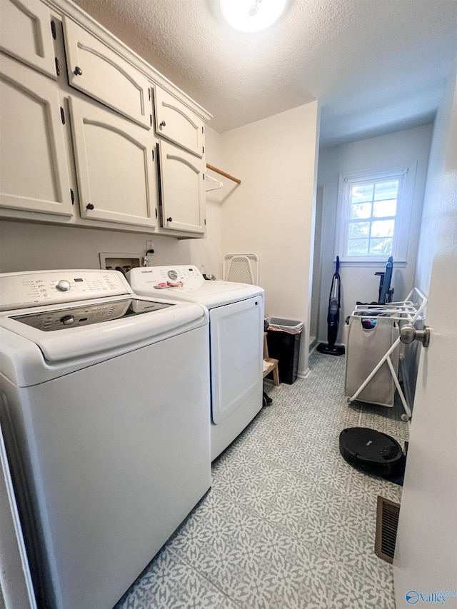 clothes washing area featuring cabinets, a textured ceiling, and washer and clothes dryer