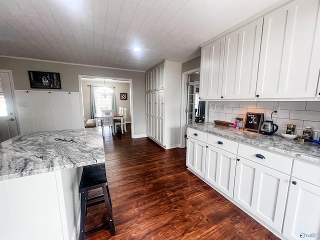 kitchen with white cabinetry, dark hardwood / wood-style flooring, light stone countertops, and tasteful backsplash