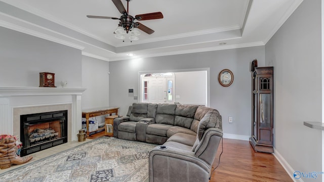 living room with crown molding, a tray ceiling, baseboards, light wood finished floors, and a ceiling fan