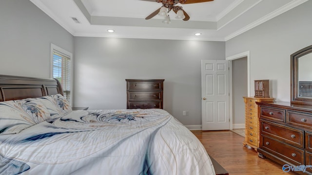 bedroom with ornamental molding, visible vents, wood finished floors, and a raised ceiling