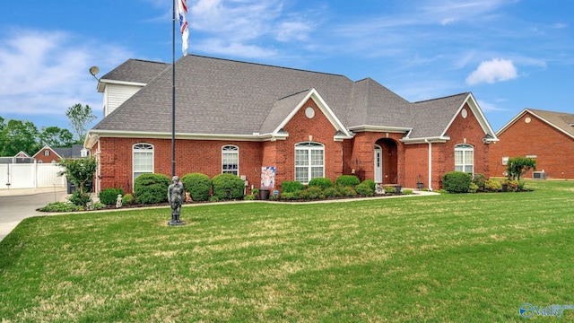 view of front of property with fence, a front lawn, a shingled roof, and brick siding