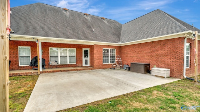 back of property featuring brick siding, a patio area, and roof with shingles