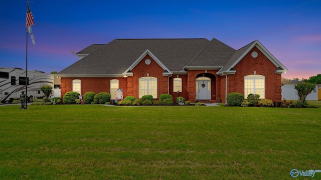 view of front of house with brick siding, a shingled roof, and a yard