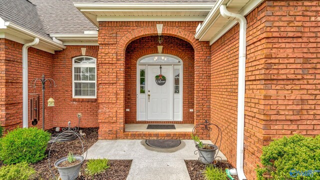 property entrance with a shingled roof and brick siding