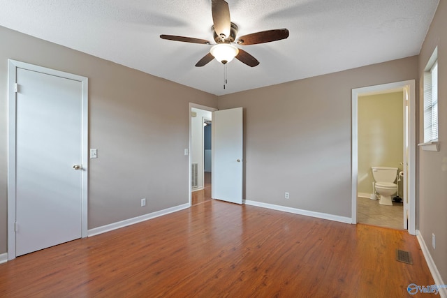 unfurnished bedroom featuring a textured ceiling, connected bathroom, light hardwood / wood-style floors, and ceiling fan