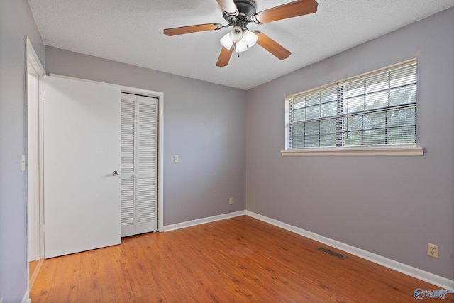 unfurnished bedroom featuring light hardwood / wood-style flooring, a closet, ceiling fan, and a textured ceiling