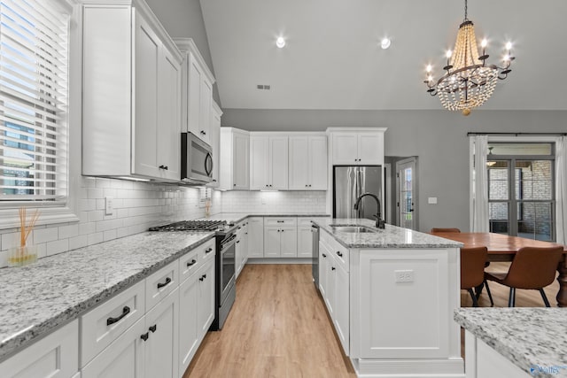 kitchen with stainless steel appliances, a chandelier, a sink, white cabinets, and lofted ceiling
