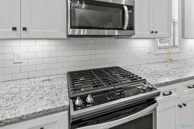 kitchen with appliances with stainless steel finishes, tasteful backsplash, white cabinetry, and light stone counters